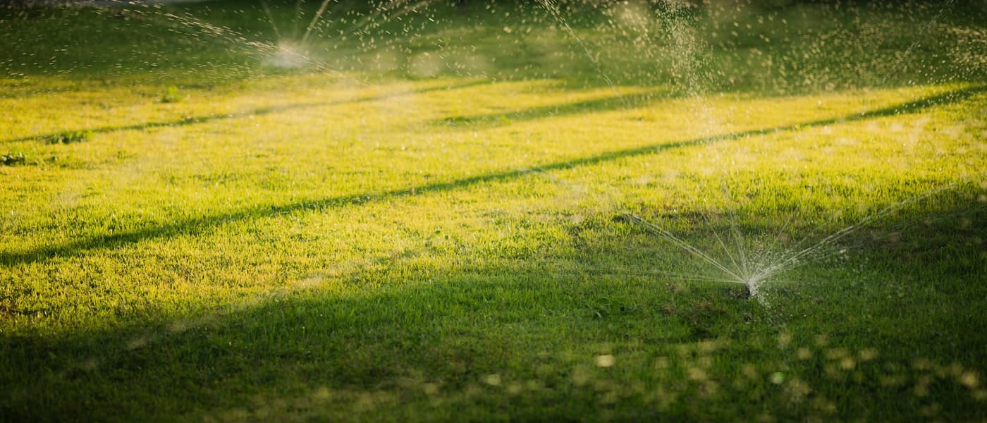 Sprinkler system watering a green lawn at golden hour