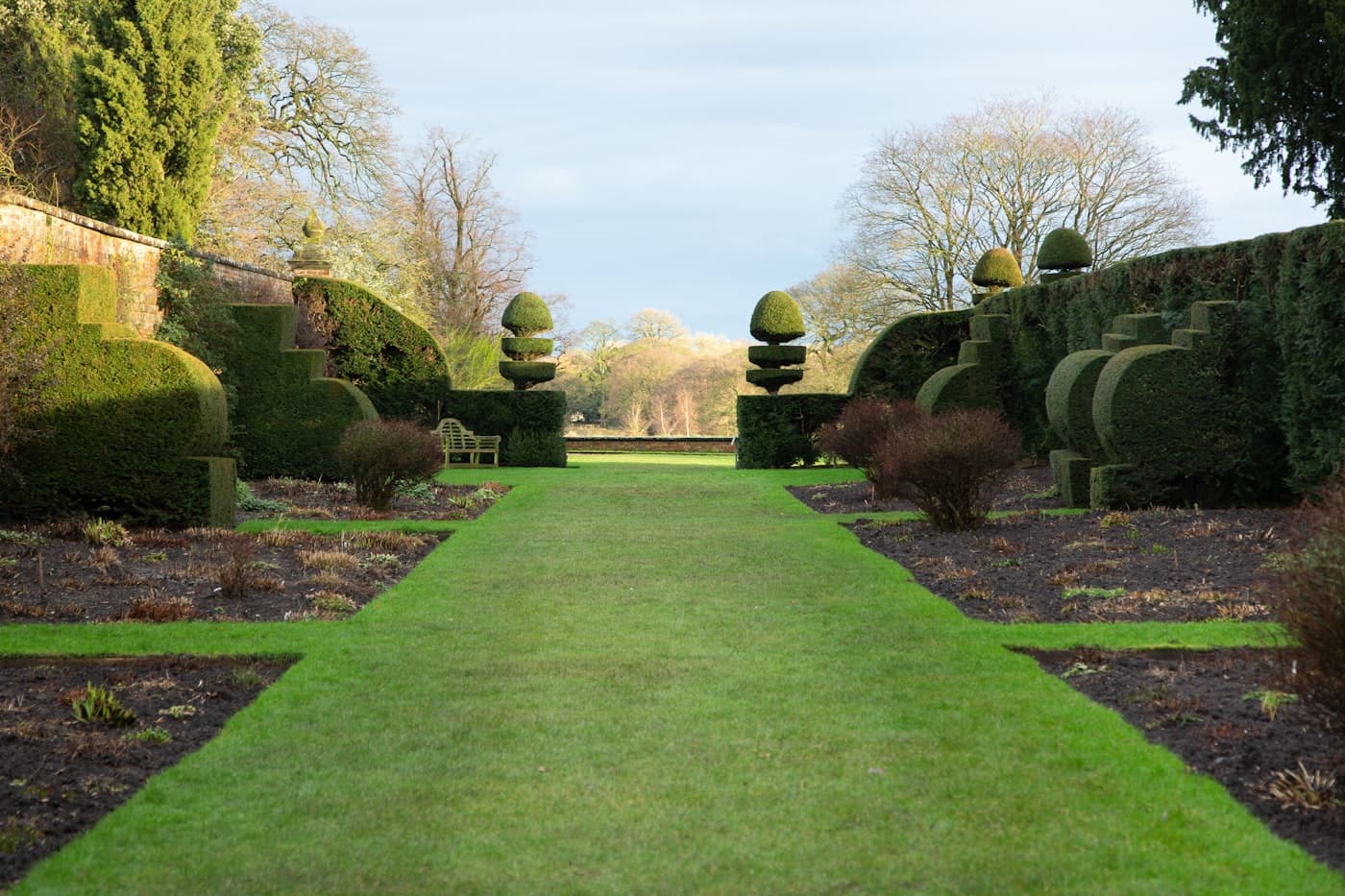 Manicured lawn bordered by shaped hedges and mature trees